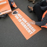Ein Protestschild mit der Aufschrift "Weg von Fossil hin zu gerecht" liegt auf dem Boden, daneben sitzt ein Mann