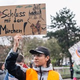 Ein Mensch mit einem Protestschild mit der Aufschrift: "Schluss mit dem Märchen"
