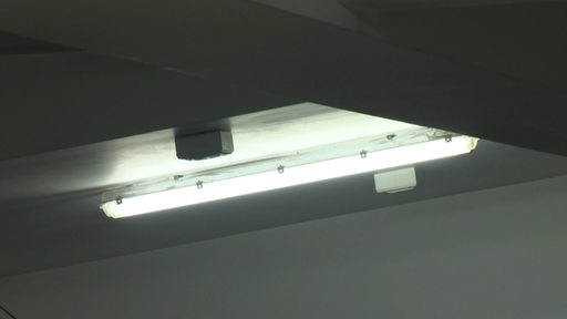 Eine Leuchtstoffröhre leuchtet an der Decke in einem dunklen Raum.