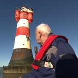 Manfred Benhof vom Förderverein ist auf einem Schiff und guckt auf den Leuchtturm Roten Sand. 