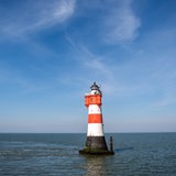 Ein rot-weißer Leuchtturm steht im Wattenmeer