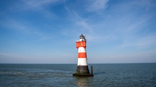 Ein rot-weißer Leuchtturm steht im Wattenmeer