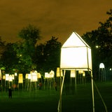 Etliche kleine beleuchtete Häuser stehen auf Stelzen in einem Park.