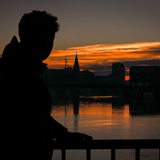 Ein Mann beobachtet den Sonnenaufgang an der Weser in Bremen, die Stadt liegt (noch) im Dunklen.