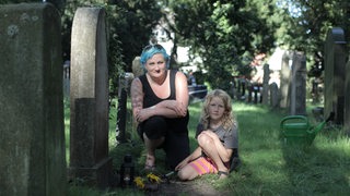 Eine Frau mit blauen Haaren sitzt mit ihrer Tochter an einem Grab auf dem jüdischen Friedhof in Hastedt