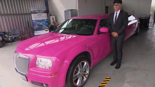Zu sehen ist eine pinke stretch Limousine mit einem Fahrer daneben.