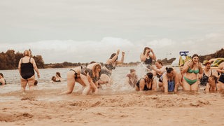 Buntes Treiben von Frauen mit Lipödem in Badekleidung am Strand