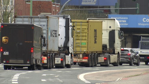 Einige LKW und Laster stehen hintereinander an einer Ampel.