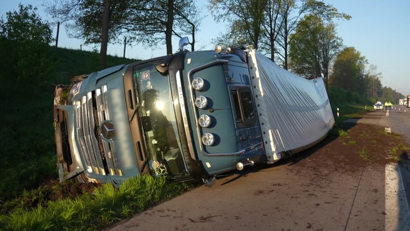 Ein Lastwagen liegt neben der Fahrbahn auf der Seite.