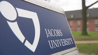 Das Logo der Jacobs University. Im Hintergrund ein Gebäude.