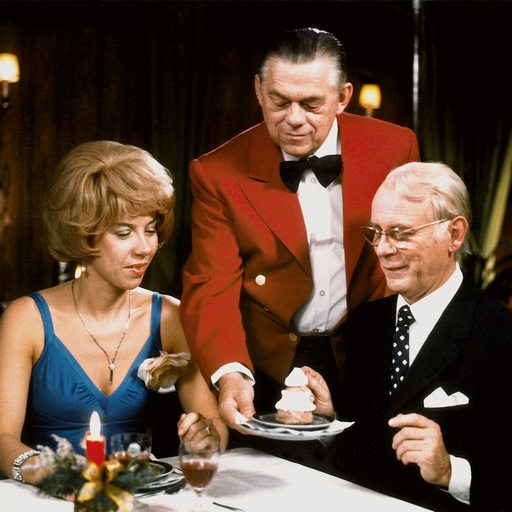 Ein Kellner serviert ein Dessert am Tisch mit Evelyn Hamann und Loriot