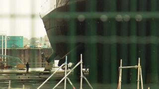 Eine Person steht vor dem Rumpf eines Schiffes in einer Werft.