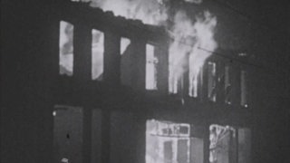 Eine schwarz weiß Aufnahme eines brennenden Hauses.