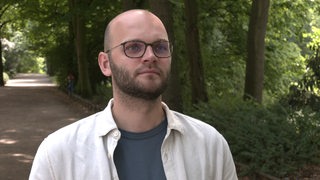 Der Sprecher des Gesundheitsressorts, Lukas Fuhrmann, auf einem Weg im Park und gibt ein Interview.