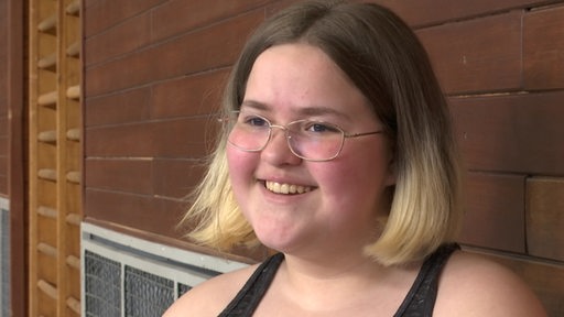 Ein Mädchen mit Brille und schulterlangen Haaren lacht.
