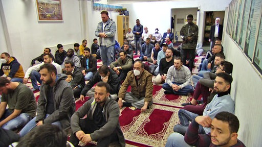 Viele Männer nehmen auf den Teppichen zum Gebet in einer Moschee Platz.