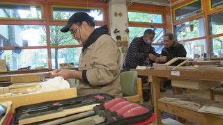 Drei Männer arbeiten an ihren Projekten in einer Holz-Werkstatt.