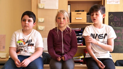 Drei GrundschülerInnen sitzen auf einem Tisch und erzählen