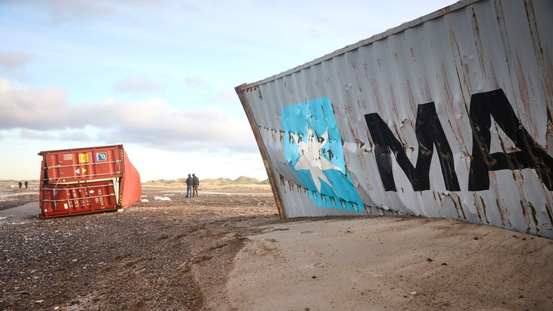 Auf einem Strandabschnitt liegen zwei angespülte Container.