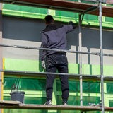 Ein Maler steht beim Streichen einer Fassade auf einem Gerüst.