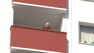 Ein älterer Mann steht alleine an seinem Balkon.