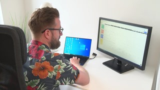 Ein Mann sitzt vor zwei Bildschirmen. Man sieht nur seinen Hinterkopf und Teile des Gesichts seitlich.
