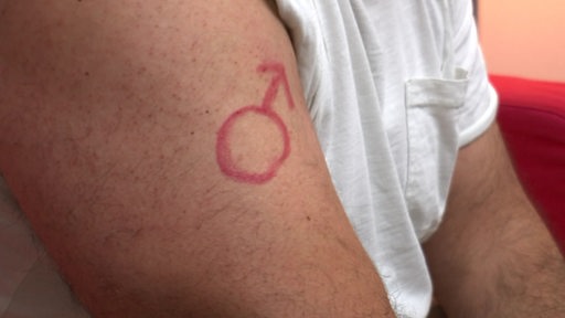 Es ist ein Oberarm eines Mannes zu sehen, auf welchem das Marssymbol gezeichnet wurde.