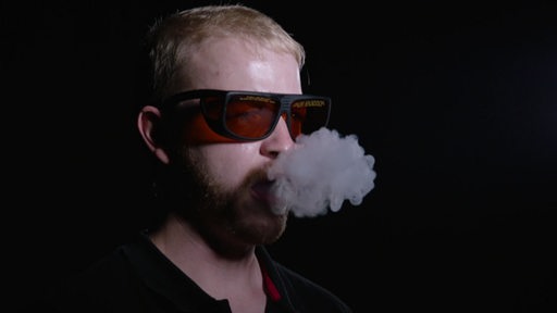 Ein Mann mit Sicherheitsbrille, dem Rauch aus dem Mund beim ausatmen steigt.