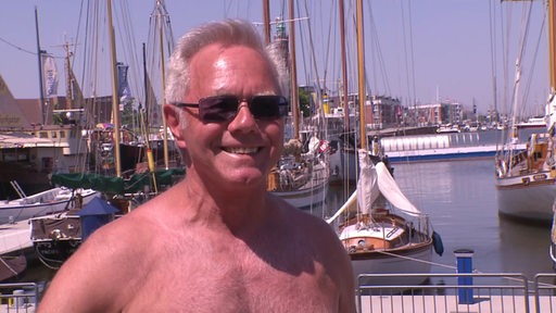 Ein Mann steht bei strahlendem Sonnenschein vor einem Anleger mit Booten.