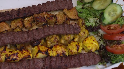 Ein Teller auf dem sich Mantu-Teigtaschen, Fleisch und Salat befinden.