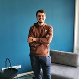 Ein junger Mann steht lachend und mit verschränkten Armen vor einer Wand.