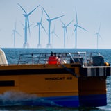 Windräder stehen im Meer. Davor ein Schiffskutter
