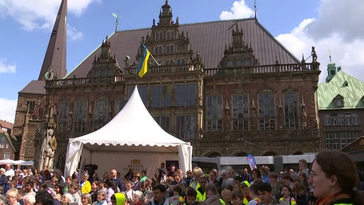 Der volle Bremer Marktplatz mit vielen Menschen und Zelten aufgebaut und dem Rathaus mit der ukrainischen Flagge im Hintergrund. 