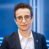 Eine Person (Masha Gessen) mit Brille und kurzen Haaren vor einem blauen Hintergrund.