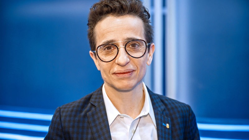 Eine Person (Masha Gessen) mit Brille und kurzen Haaren vor einem blauen Hintergrund.