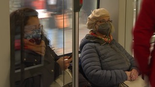 Zwei Damen sitzen mit Mund-Nasen-Schutz-Masken in einer Bahn.