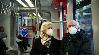 Zwei ältere Leute auf einer Sitzbank einer Straßenbahn.