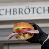Ein Matjes Fischbrötchen wird vor einem Schild gehalten