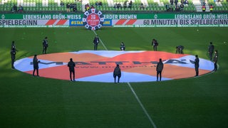 Menschen halten ein rundes Banner vom Bauunternehmen Matthäi im Mittelkreis des Weserstadions.