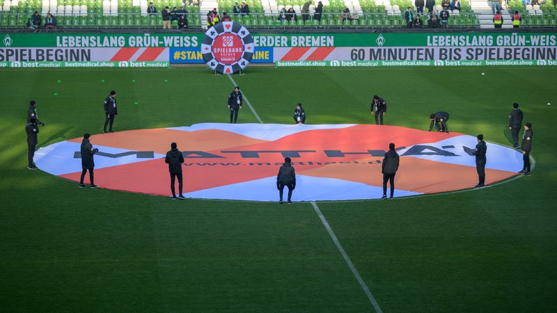 Menschen halten ein rundes Banner vom Bauunternehmen Matthäi im Mittelkreis des Weserstadions.