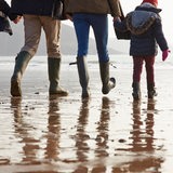 Eine Familie mit 2 Kindern macht in Gummistiefeln eine Wattwanderung.