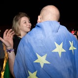 Ein Mann trägt eine Europaflagge über den Schultern und unterhält sich mit einer lächelnden Frau.