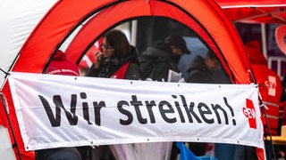 Ein Banner mit der Aufschrift „Wir streiken!“ ist am Stand der Gewerkschaft Erziehung und Wissenschaft (GEW) bei einer zentralen Warnstreikkundgebung zu sehen.