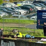 Menschen sitzen mit Warnwesten auf Gleisen. Um sie herum stehen drei Polizisten