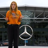 Eine Frau steht vor einem Fotos des Mercedes-Stern.