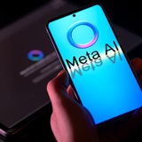 Das Logo von Meta AI auf einem Smartphone, im Hintergrund ein Laptop