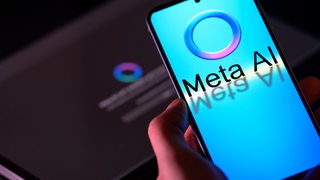 Das Logo von Meta AI auf einem Smartphone, im Hintergrund ein Laptop