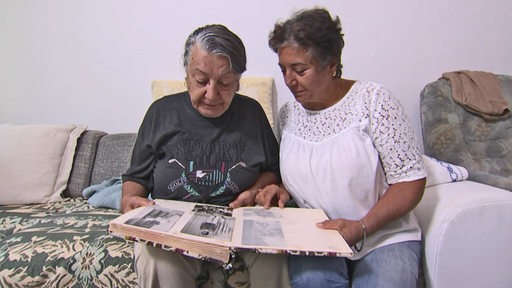 Zwei Personen schauen gemeinsam in ein Fotoalbum mit schwarz-weisß Bildern.