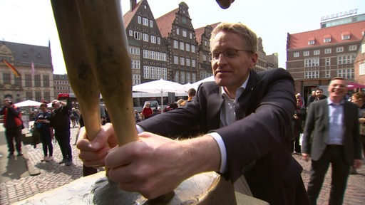 Schleswig-Holsteins Ministerpräsident Daniel Günther zu Besuch in Bremens Innenstadt. Traditionsgemäß berührt er die Beine der goldenen Eselstatue.