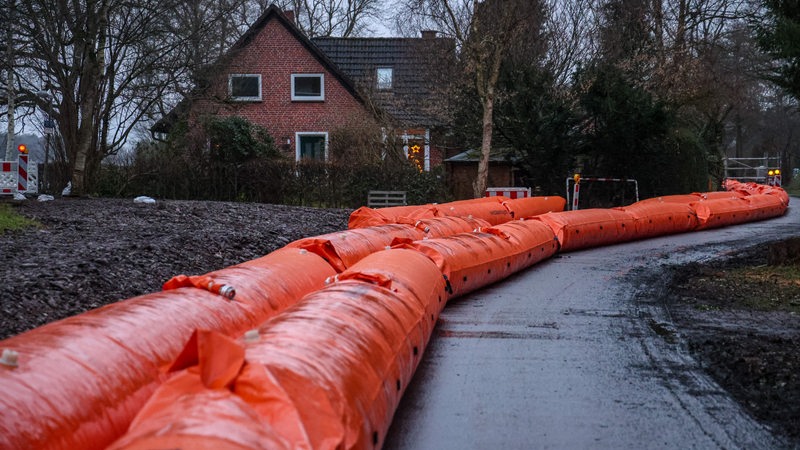 Ein mobiler Hochwasserschutz aus rotem Plastik liegt neben einem Deich.